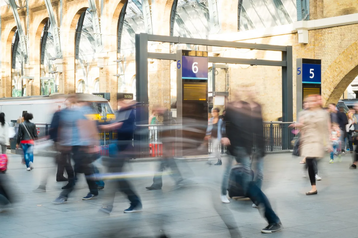 Motion-blurred commuters walking through a train station with arched brick ceilings and platform gates