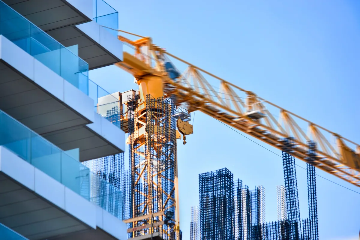 Yellow construction crane and glass-paneled building against a clear blue sky at a construction site